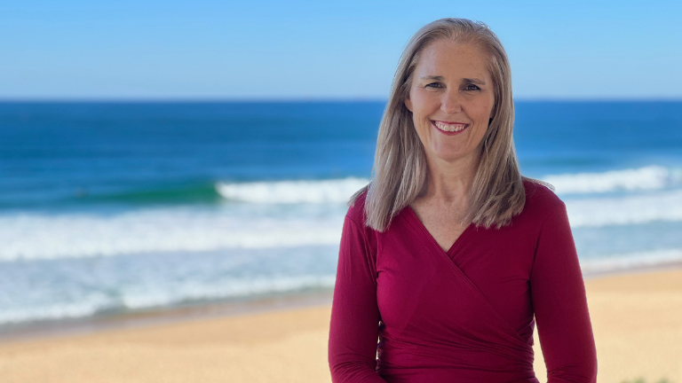 Professor Suzanne Snodgrass - woman with long hair standing smiling in front of a beach