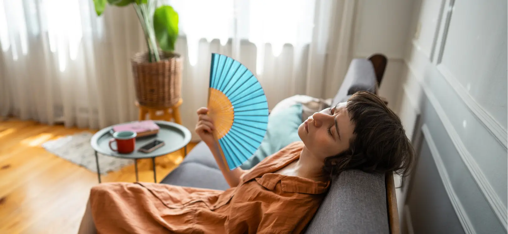 Woman sits on a lounge exhausted and using a fan to cool herself during a heatwave