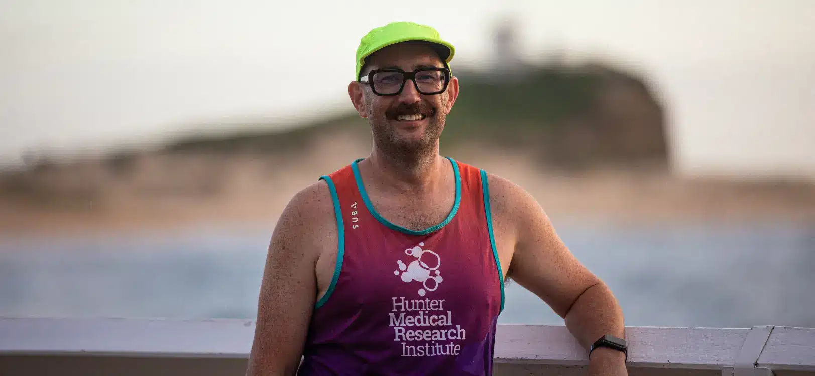 Heavy lifting for medical research Mike Collins runs Sisyphus Challenge for HMRI | Mike Collins stands in front of Nobby's Beach wearing his team HMRI Hill to Harbour running singlet