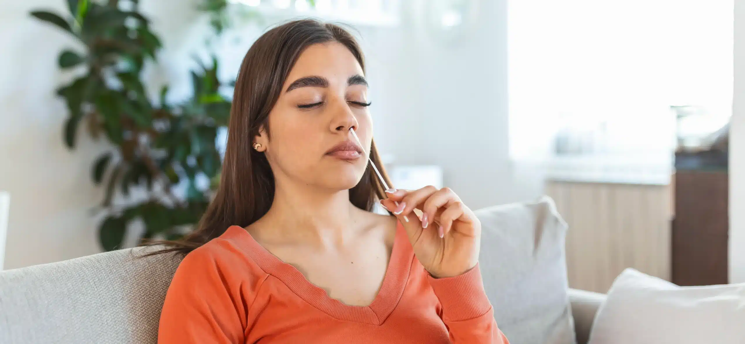 Could at-home nasal swabs help spot the next virus outbreak or pandemic | HMRI A woman sits on her lounge within her home using a nasal swab in her nostril